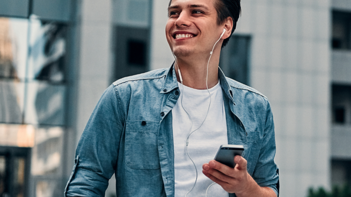 Uśmiechnięty chłopak w niebieskiej koszuli trzymający w ręku telefon komórkowy