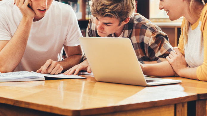 Grupa trzech studentów siedząca przy biurku